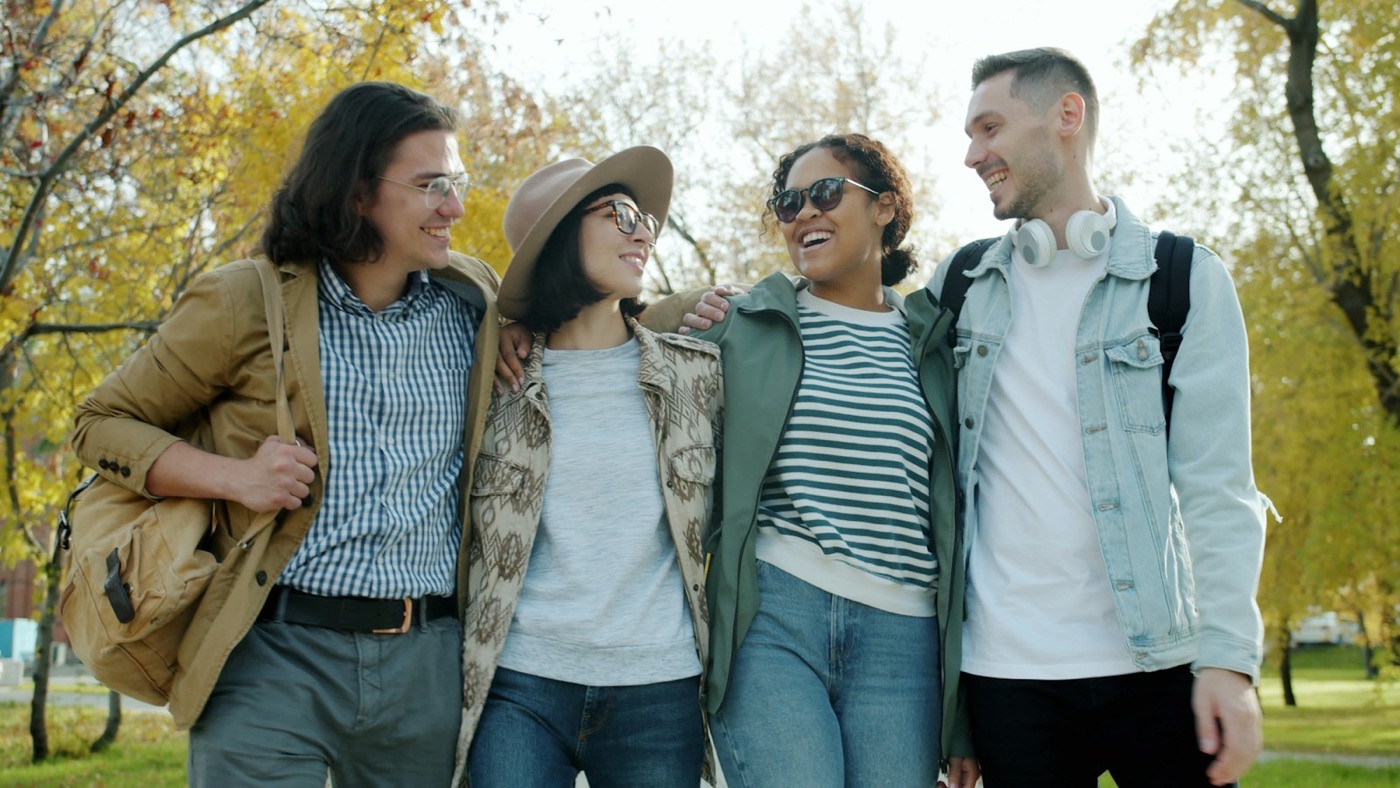 Four friends laughing together on a walk through a sunny park