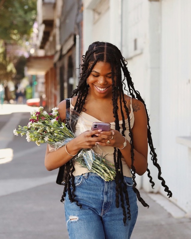 A smiling woman checks her phone while walking down a sunny street
