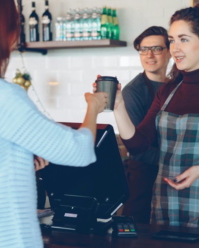 A barista hands a coffee to a customer across the counter